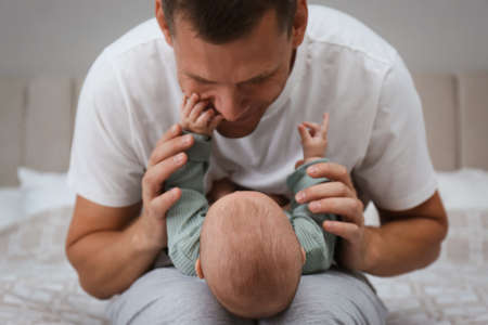 Happy father holding his cute baby on bed at home