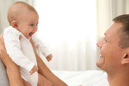 Happy father holding his cute baby on bed at home