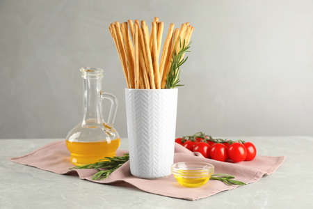 Delicious grissini sticks, oil, rosemary and tomatoes on gray marble table