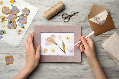 Woman making beautiful herbarium with pressed dried flower at wooden table, top view.の写真素材