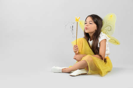 Cute little girl in fairy costume with yellow wings and magic wand on light background. Space for textの写真素材