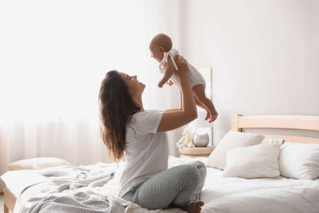 Happy young mother with her cute baby on bed at homeの写真素材