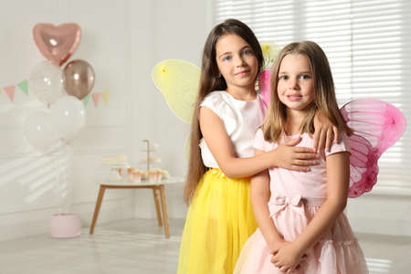 Cute little girls wearing fairy costumes in decorated room. Space for text
