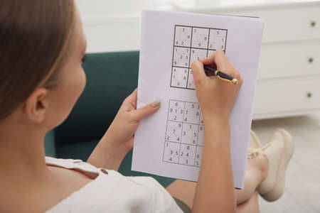 Young woman solving sudoku puzzle on sofa indoors, closeupの写真素材