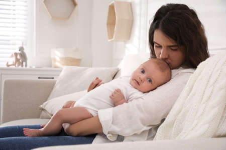 Young mother with her cute baby on sofa at homeの写真素材