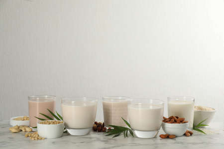 Different vegan milks and ingredients on white marble table. Space for text