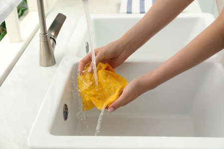 Woman washing beeswax food wrap under tap water in kitchen sink, closeup