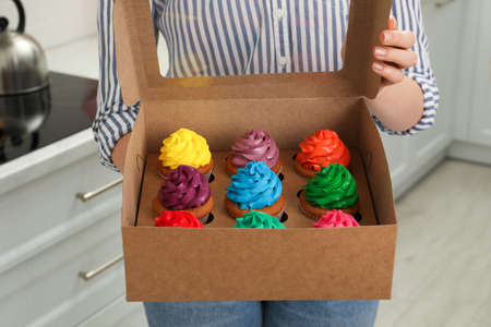 Woman holding box with delicious colorful cupcakes indoors, closeupの写真素材