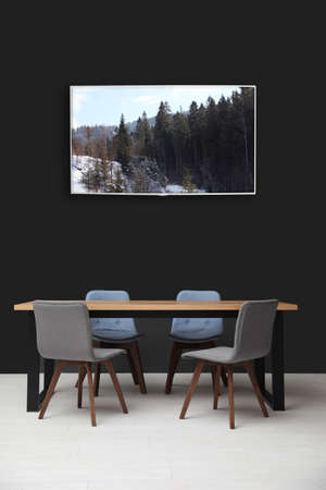 Modern wide screen TV on black wall in room with stylish furniture