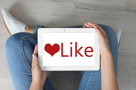 Woman using tablet with word Like on screen indoors, top viewの写真素材