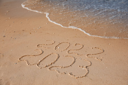 2022 and 2023 written on sand at beach. New Year celebration