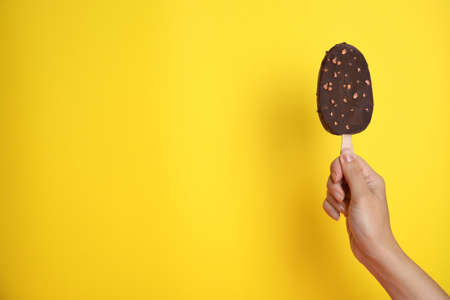 Woman holding ice cream glazed in chocolate on yellow background, closeup. Space for textの写真素材