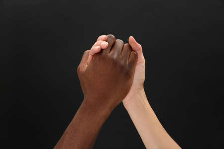 Woman and African American man clasping hands on black background, closeupの写真素材