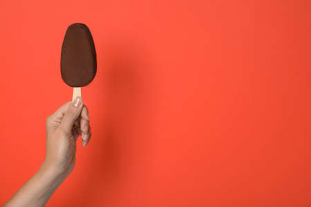 Woman holding ice cream glazed in chocolate on red background, closeup. Space for textの写真素材