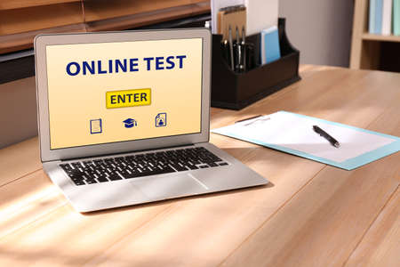 Laptop with online test on wooden desk in officeの写真素材