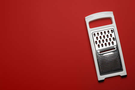 Modern grater on red background, top view. Space for text