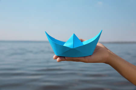 Child holding blue paper boat near river, closeupの写真素材