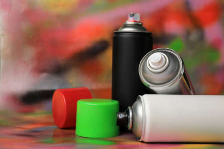 Cans of different graffiti spray paints on color background