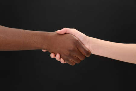 Woman and African American man shaking hands on black background, closeupの写真素材