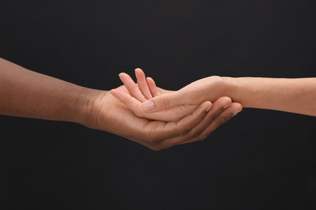 Woman and African American man holding hands on black background, closeupの写真素材