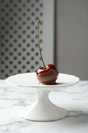 Sweet chocolate dipped cherry on white marble table