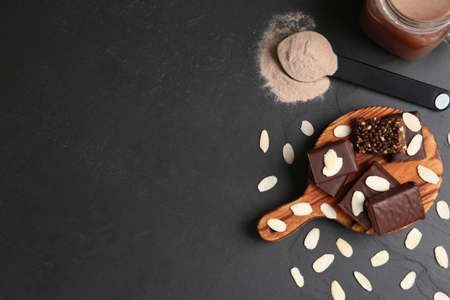 Different energy bars, almond flakes, protein cocktail and powder on black table, flat lay. Space...