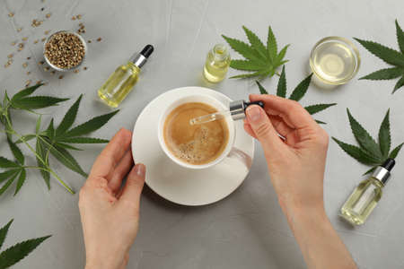 Top view of woman dripping THC tincture or CBD oil into coffee at light gray table, closeupの写真素材