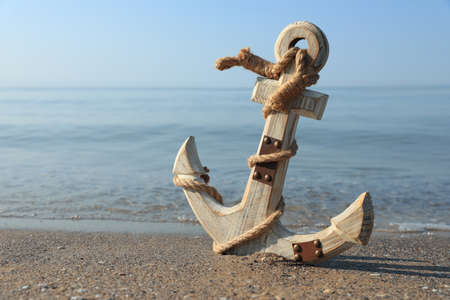 Wooden anchor with rope on sand near sea. Space for text