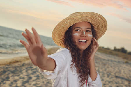 Happy African American woman with sun protection cream on face at beachの写真素材