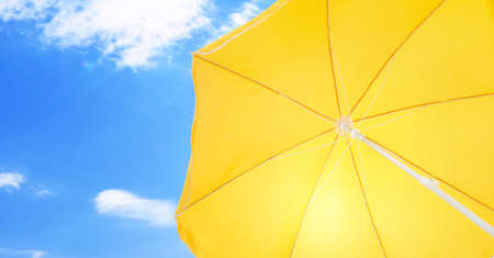 Open big yellow beach umbrella and beautiful blue sky with white clouds on background