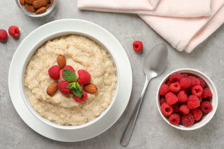 Tasty oatmeal porridge with raspberries and almond nuts served on light gray table, flat layの写真素材