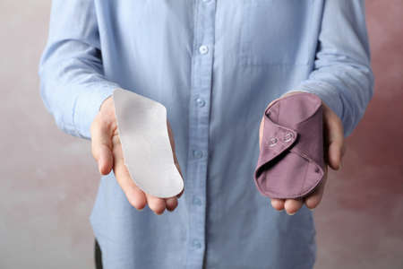 Woman holding disposable and reusable cloth menstrual pads on gray background, closeupの写真素材