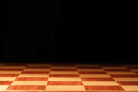 Checkered chessboard on dark background, closeup. Space for textの写真素材