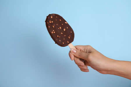 Woman holding ice cream glazed in chocolate on light blue background, closeup