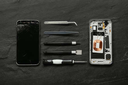 Damaged smartphone and repair tools on black background, flat layの写真素材