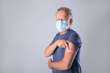Senior man in protective mask pointing at arm with bandage after vaccination on gray background. Space for textの写真素材