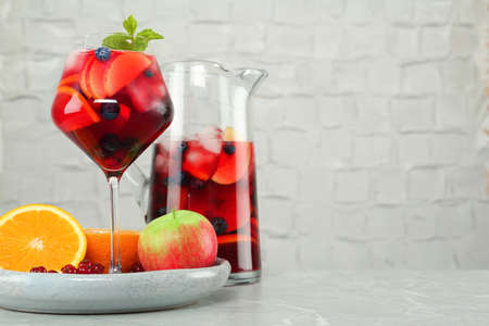 Glass and jug of Red Sangria with fruits on table near white brick wall, space for textの写真素材
