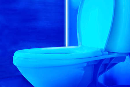 Toilet bowl in public restroom lit with UV blue light, closeup viewの写真素材