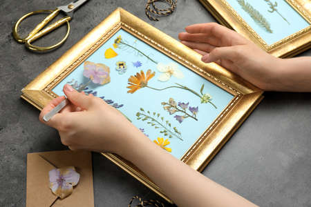 Woman making beautiful herbarium with pressed dried flower at black table, closeup