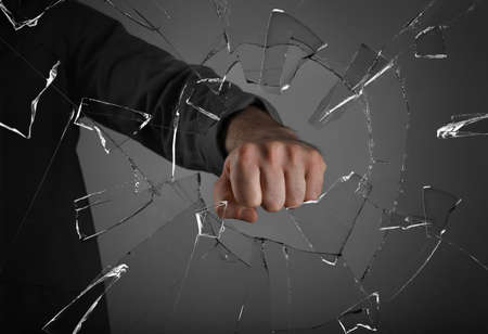 Man breaking window with fist on gray background, closeup