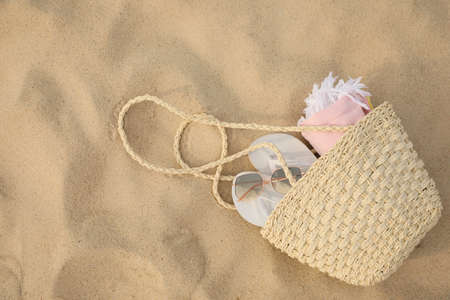 Beach bag with flip flops, towel and sunglasses on sand, top view. Space for textの写真素材