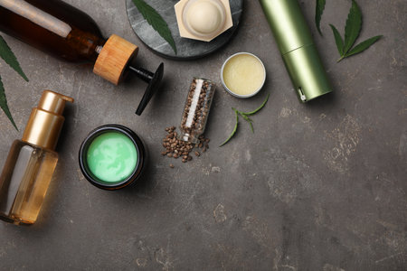 Hemp cosmetics and green leaves on gray table, flat lay. Space for textの写真素材