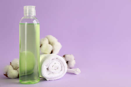 Cotton swabs, towel, dry flowers and makeup removal product on violet background. Space for text
