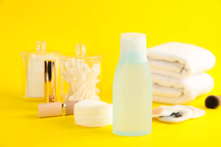 Dirty cotton pads, lipstick, toiletries and makeup removal product on yellow background