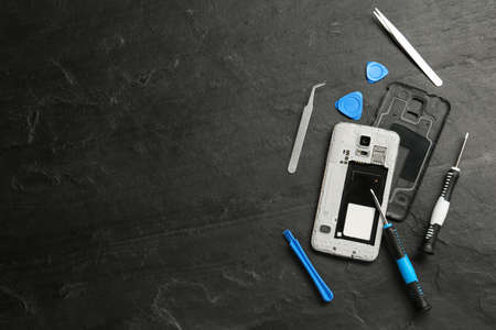 Damaged smartphone and repair tools on black background, flat lay. Space for textの写真素材