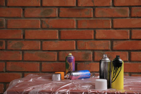 Used cans of spray paints on table near brick wall, space for text. Graffiti supplies