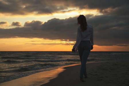 Woman walking on sandy beach during sunset, back view