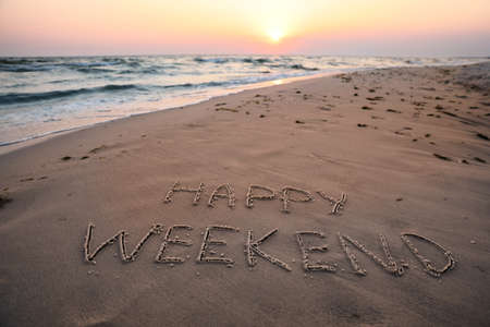Text Happy Weekend written on sandy beach at sunsetの写真素材