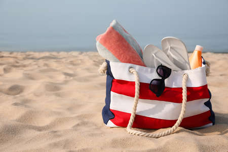 Beach bag with flip flops, towel, sunglasses and sunscreen on sandy seashore, space for textの写真素材