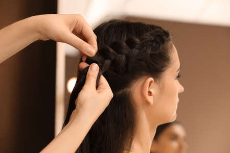 Professional stylist braiding client's hair in salon
